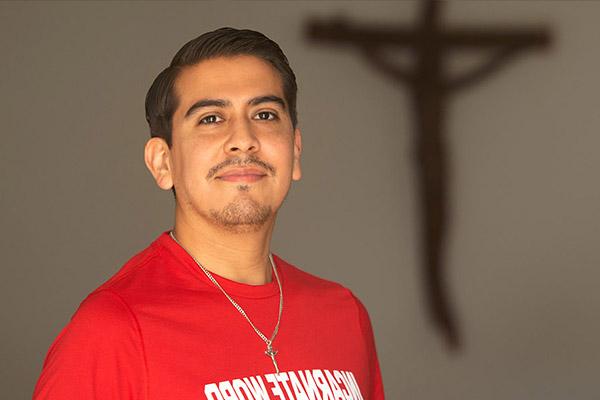 Pastoral Institute student posing in front of a wall with a crucifix on it